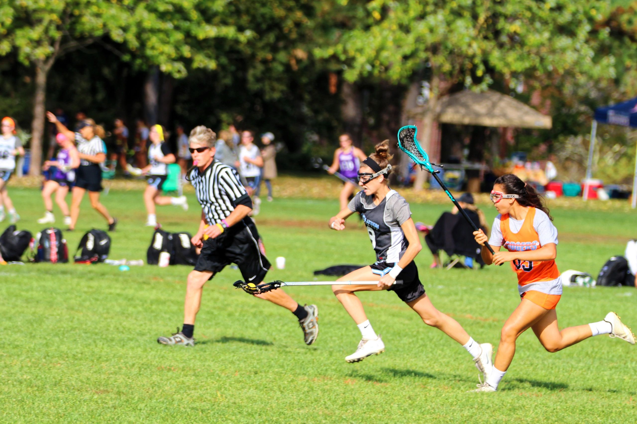 Lacrosse players competing with a referee in the background.