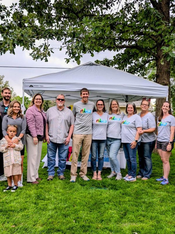 Group of people posing outdoors under tents on a grassy area.