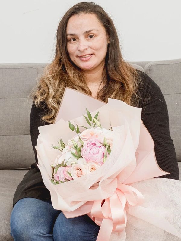 A woman sitting on a couch holding a bouquet of pink and white flowers.