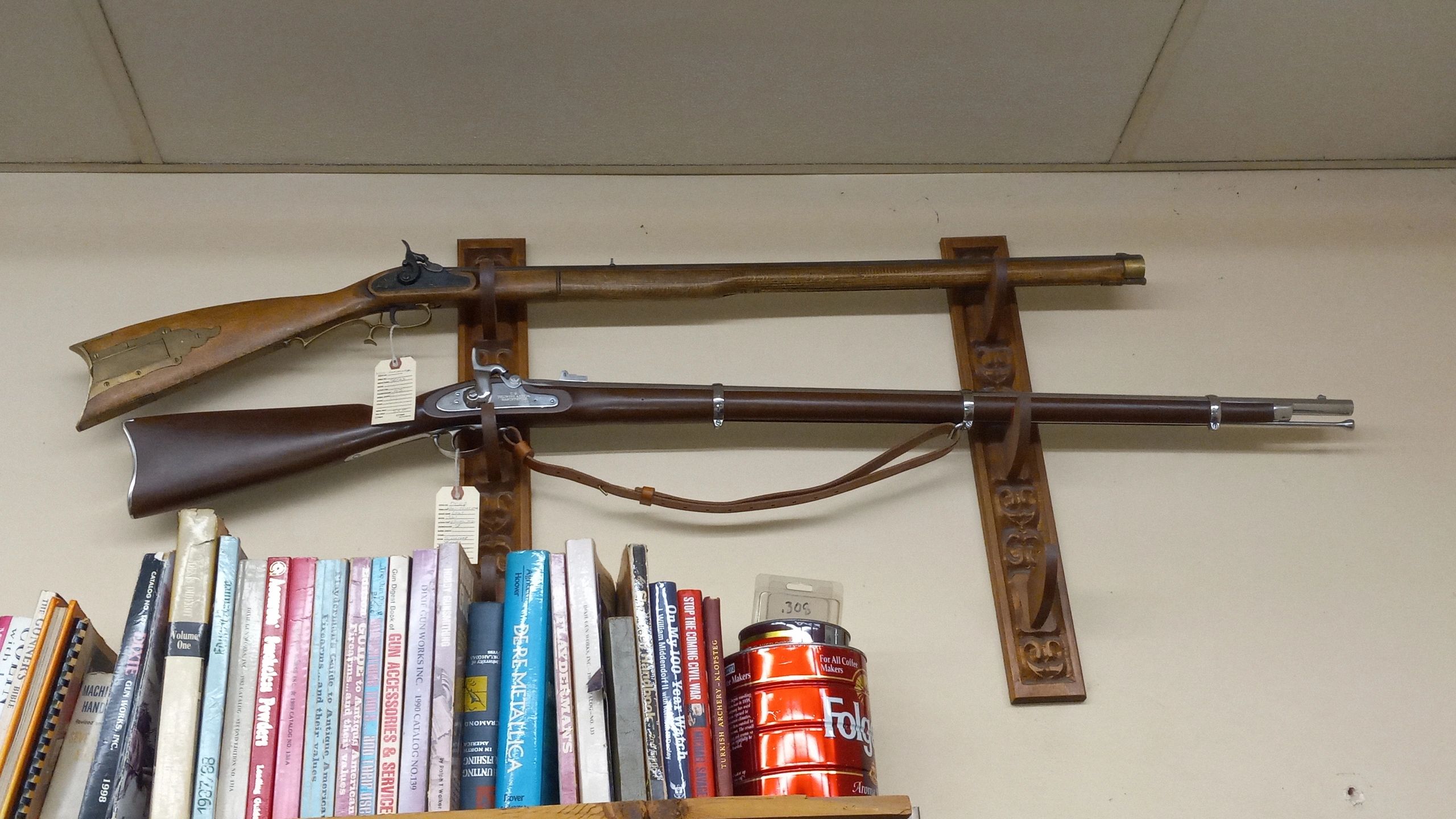 Two antique rifles displayed above a bookshelf filled with books and items.