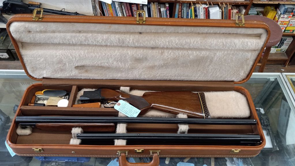 A disassembled shotgun neatly stored in a cushioned carrying case with compartments.