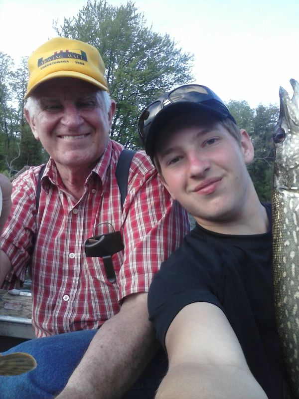A young man and an older man smiling while holding a fishing catch outdoors.