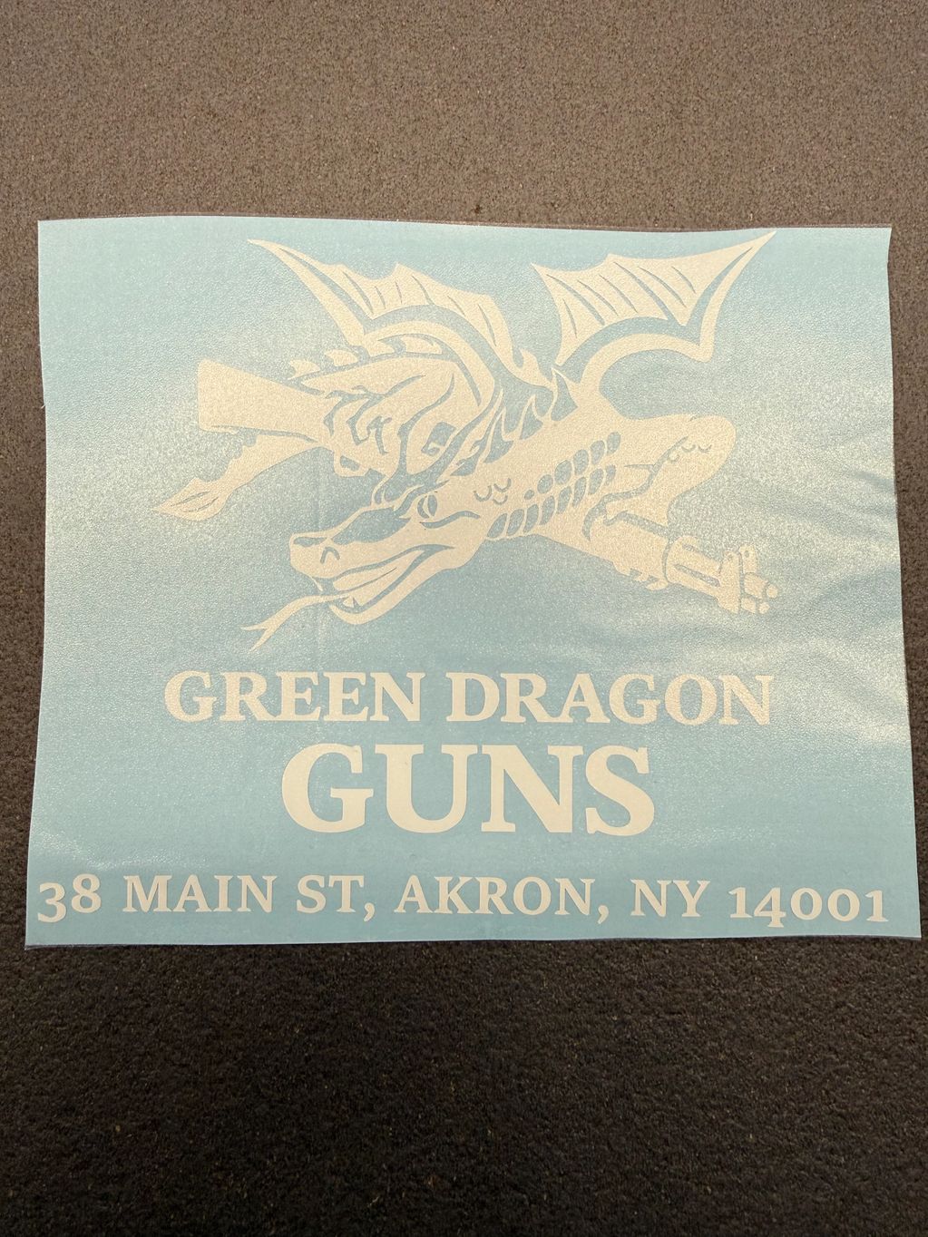 Logo for Green Dragon Guns with a dragon holding guns and an address in Akron, NY.