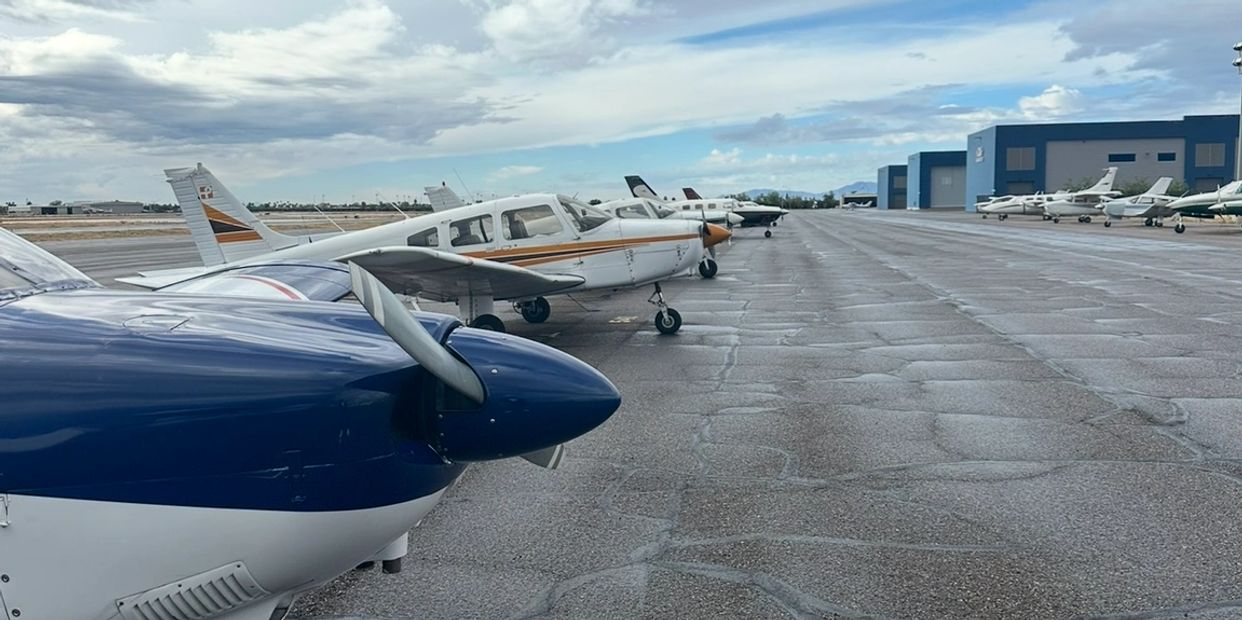 Row of small airplanes parked on a wet tarmac under a cloudy sky.