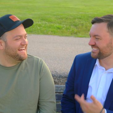 Two men sitting outdoors, smiling and chatting warmly.