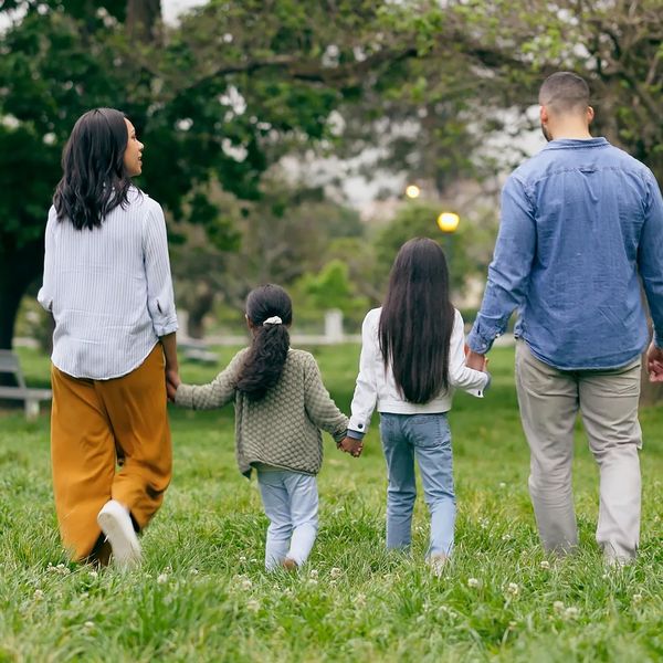Image of a father and mother holding hand with their two daughters walking through an area of grass 