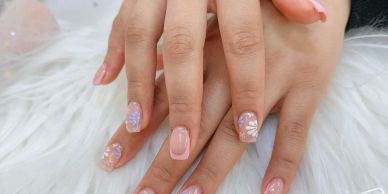 Hands with pink and floral nail art on a white furry surface.