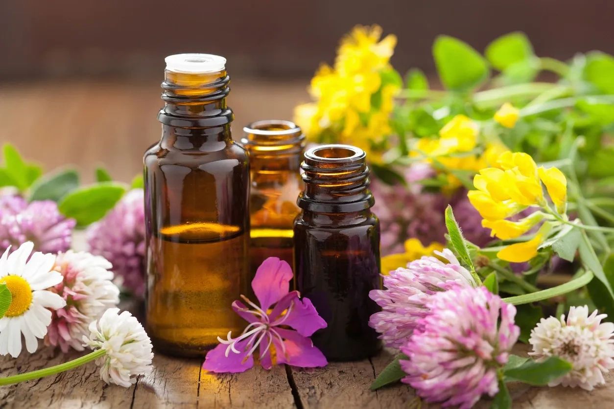 Amber glass bottles surrounded by colorful flowers on a wooden surface.