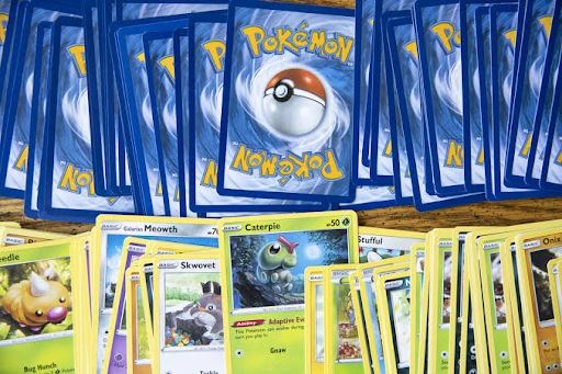 Pokémon TCG cards on wood: face-up Weedle, Meowth, Skwovet, Caterpie; many face-down with Poké Ball 