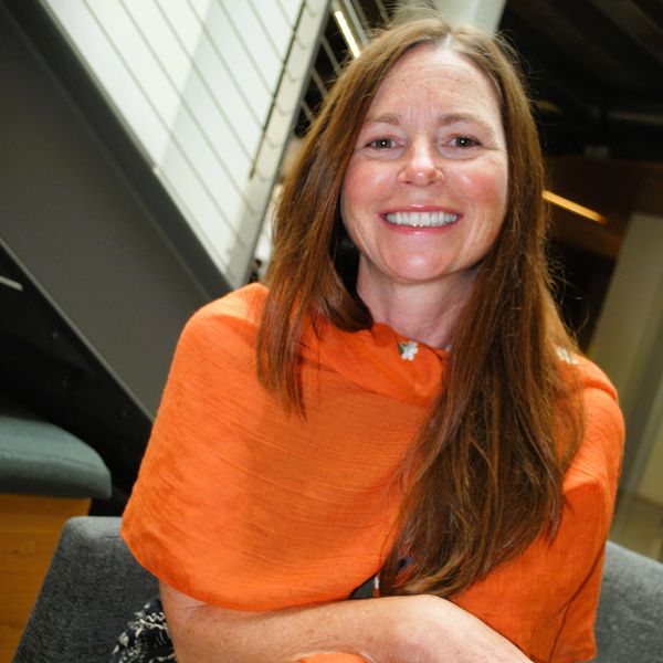 Smiling woman with long hair in an orange shawl indoors.
