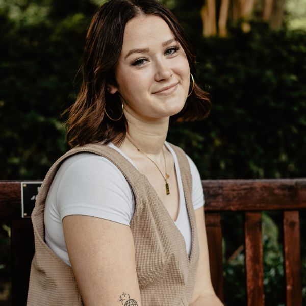 Young woman with hoop earrings smiling gently while sitting outdoors.