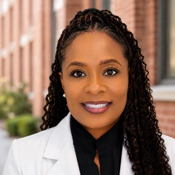 Smiling woman with braided hair in a white blazer.