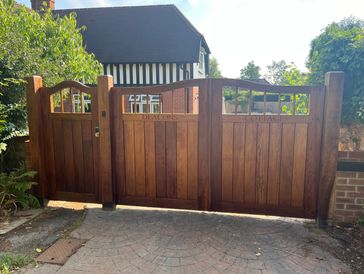 Wooden gates with 'Deacons Cottage' carved, in front of a charming brick and timber house.