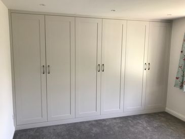 A large, light gray built-in wardrobe with six doors and silver handles.