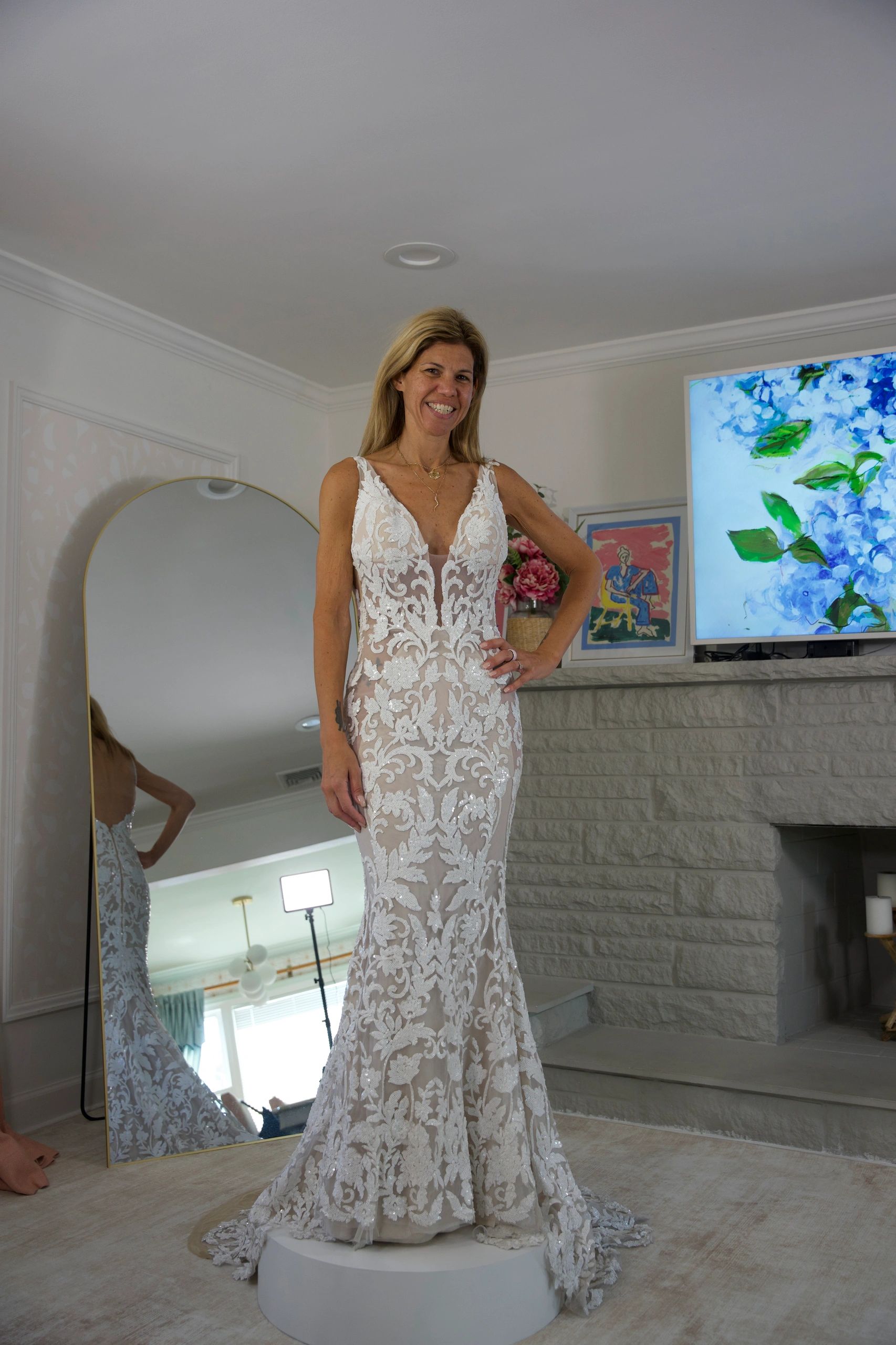 Woman in a white floral lace wedding dress smiling.