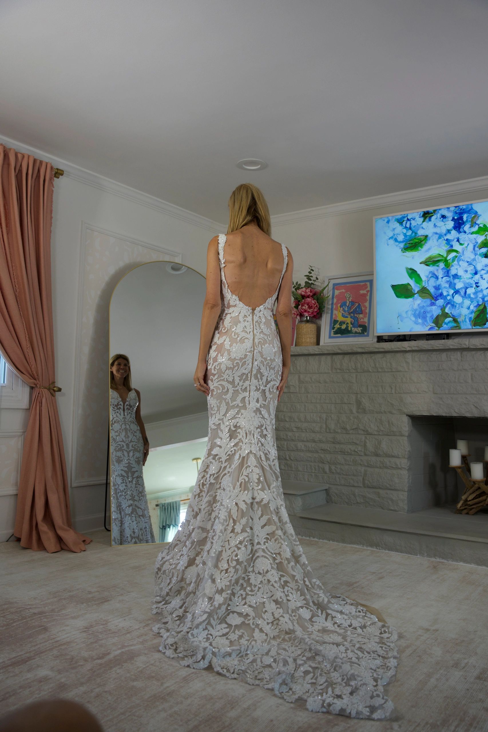 Woman in an elegant lace wedding dress looking in a full-length mirror.