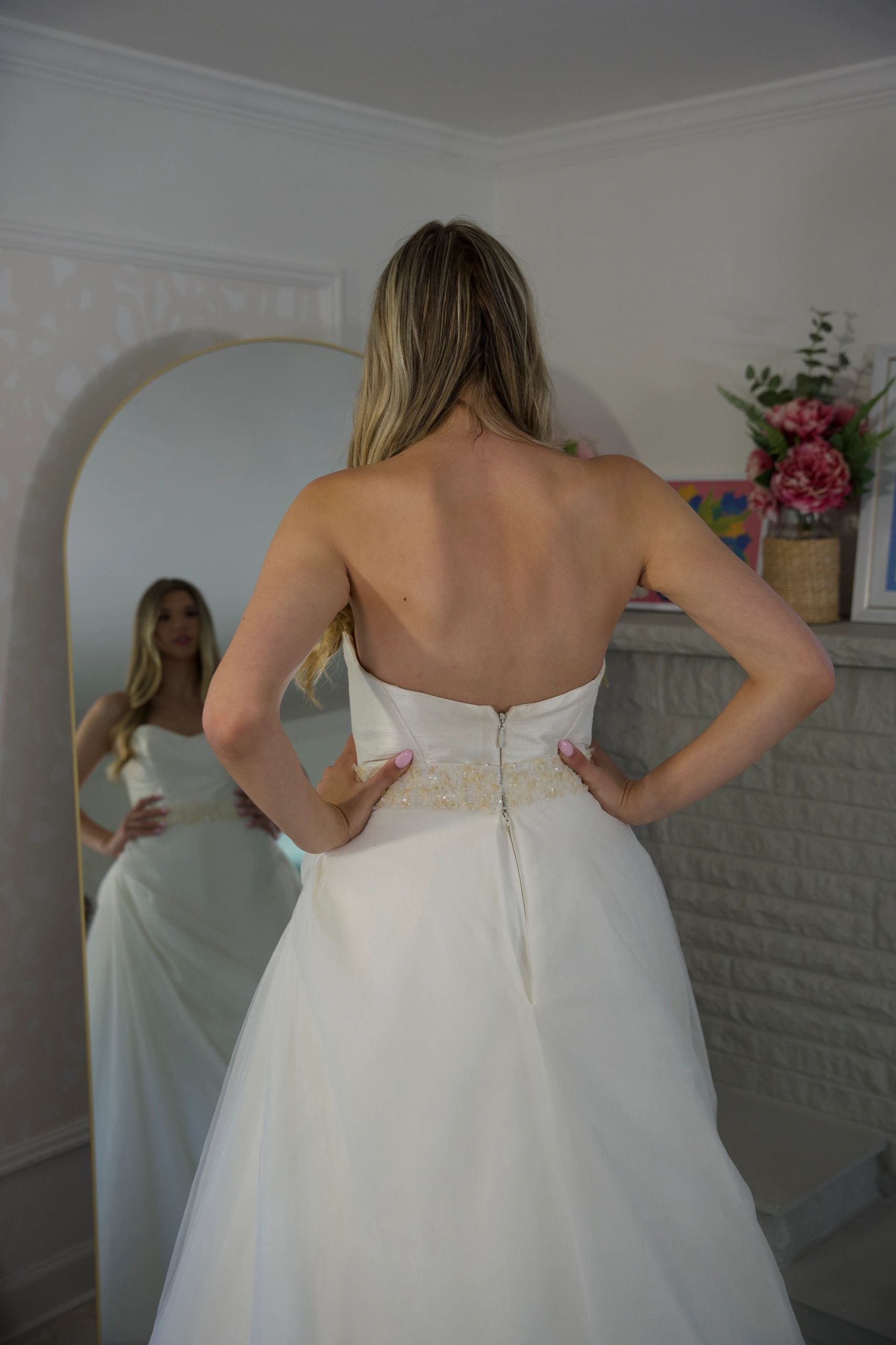 Woman in white dress looking at her reflection in a mirror.