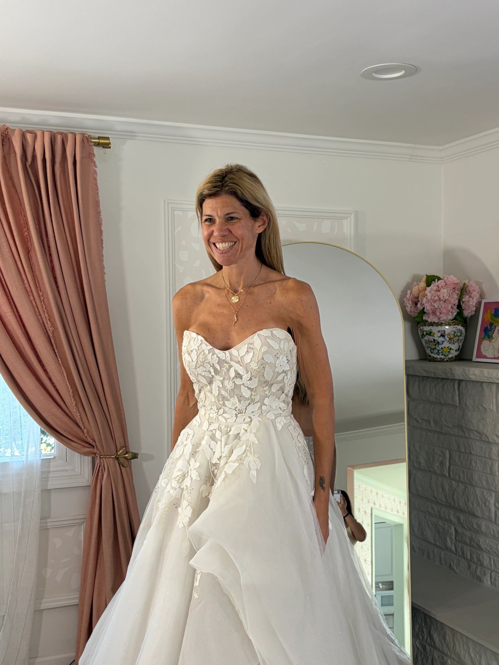 Smiling woman in a strapless white wedding dress indoors.