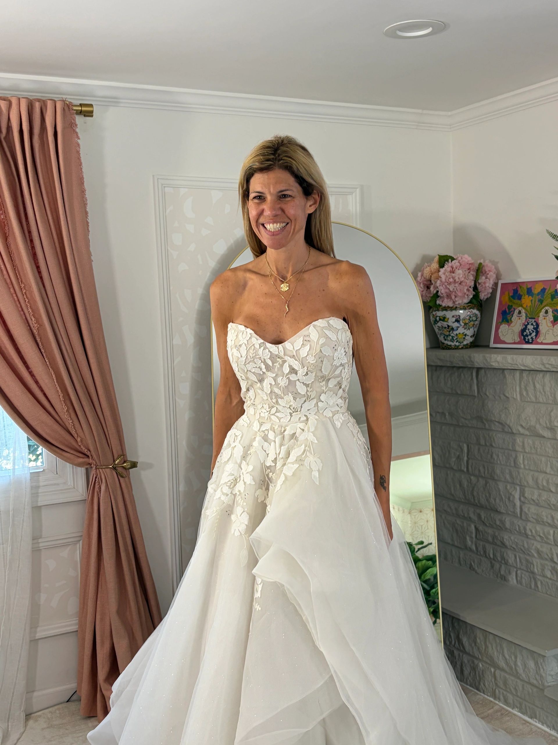 Woman in a white strapless wedding dress smiling indoors.