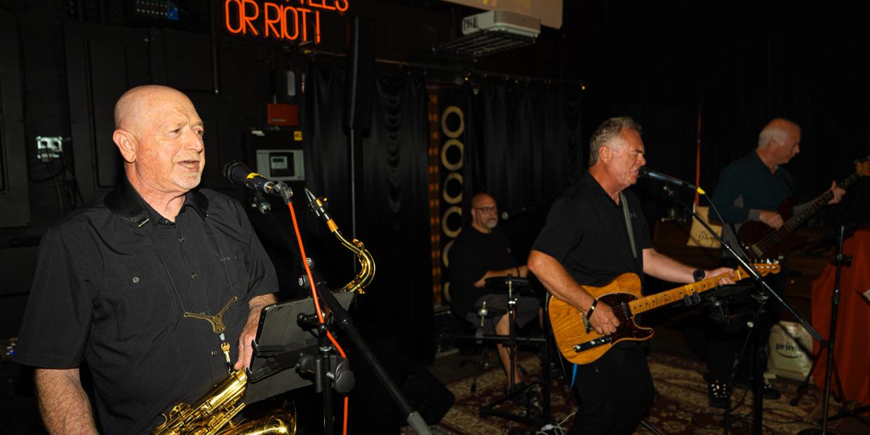Band performing live with saxophone, guitar, bass, and drums.