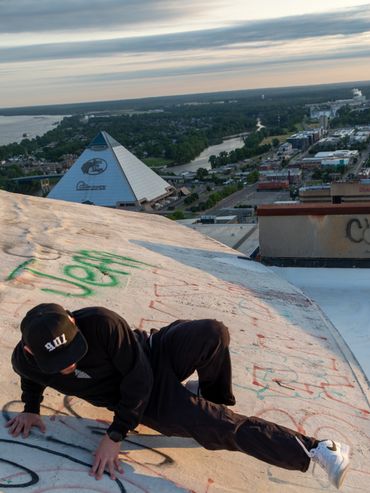 Person in black outfit climbing a graffiti-covered rooftop with a cityscape in the background.