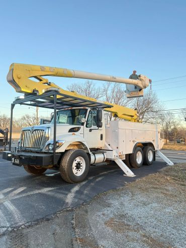 A white utility bucket truck with an extended yellow boom and worker in the bucket.