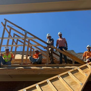 Construction workers posing on a wooden roof frame under a clear blue sky.