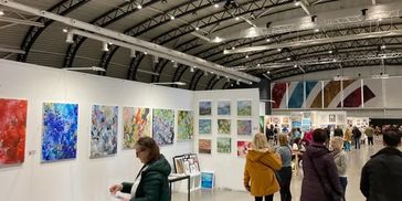 People explore colorful artwork at an indoor art exhibition.