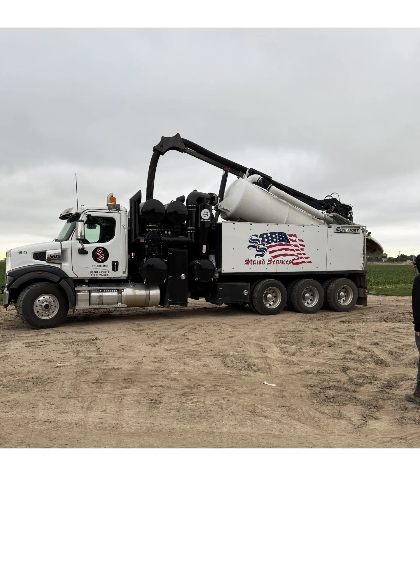 Large white and black vacuum truck with American flag logo on a dirt field.