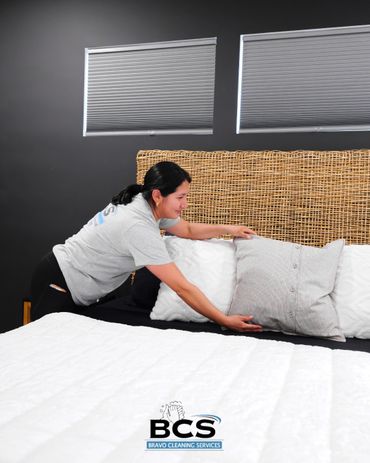 Woman making a bed with pillows in a clean room.