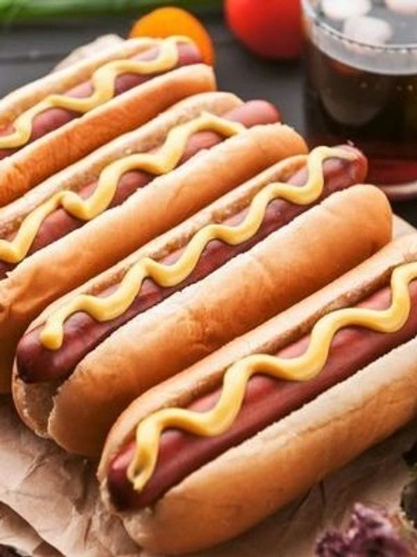 Four hot dogs with mustard in buns, served with a drink.