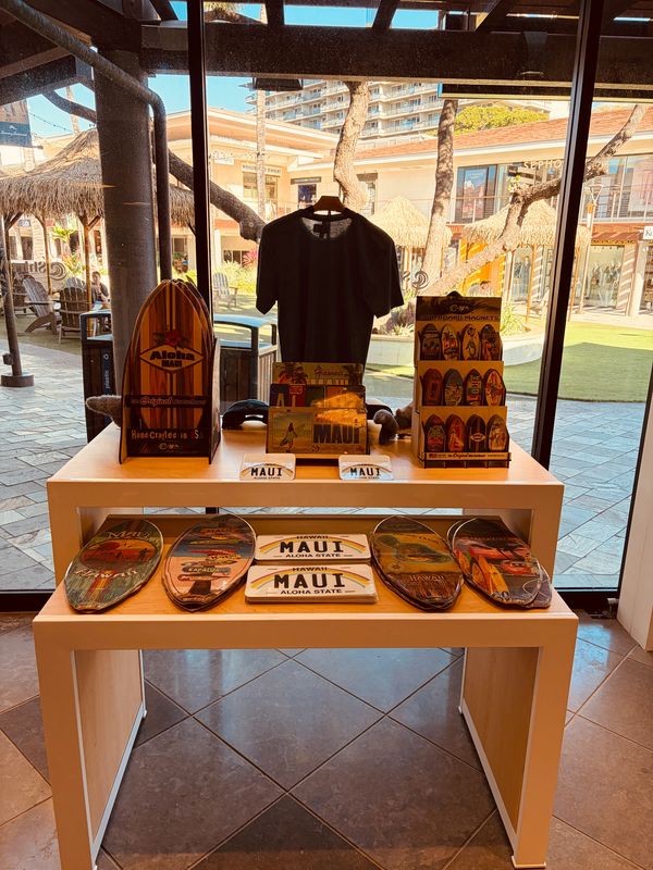 Maui-themed souvenirs and a black shirt displayed on a table in a shop.