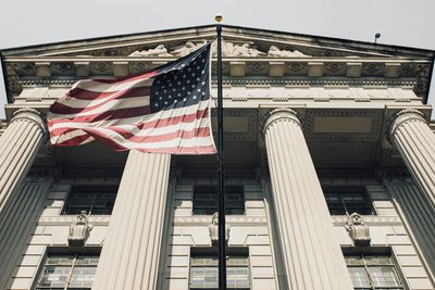 American flag waving in front of a classical government building with large columns.