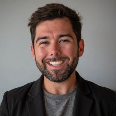 Smiling man with a beard wearing a black blazer and gray shirt.