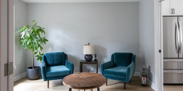 Modern living room with two teal chairs and a round wooden table.