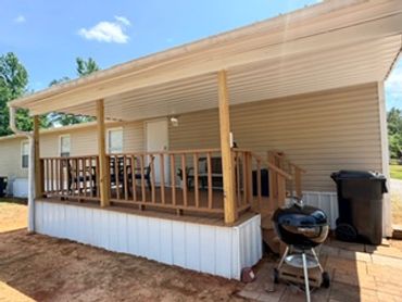 A mobile home porch with wooden railings and a charcoal grill outside.