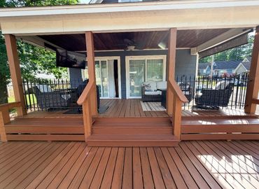 A cozy wooden porch with seating and a ceiling fan on a sunny day.