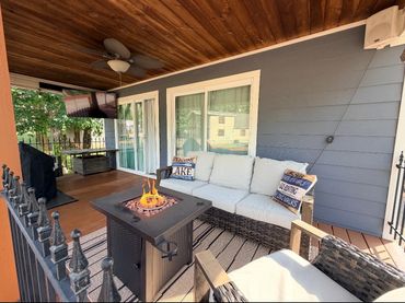 Cozy outdoor patio with sofa, fire pit, and TV under a wooden ceiling.