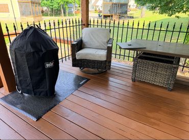 Covered grill, cushioned chair, and table on a wooden porch.
