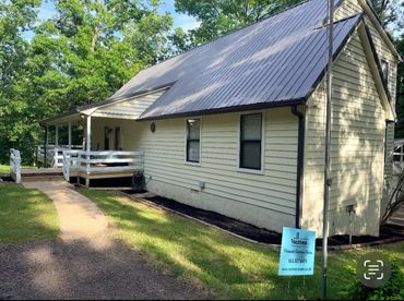 A quaint yellow house with a metal roof and a small porch surrounded by trees.