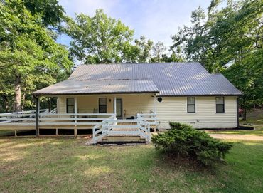 Single-story house with a metal roof and white wooden ramp surrounded by trees.