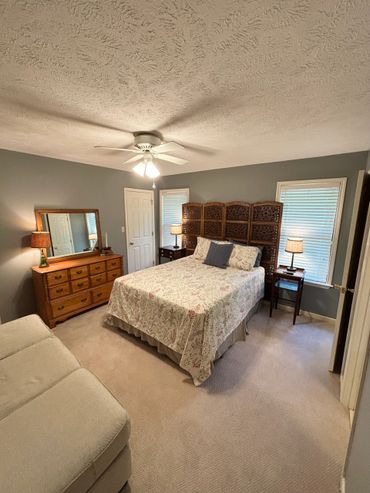 Cozy bedroom with a wooden dresser, bed with floral bedding, and soft lighting.