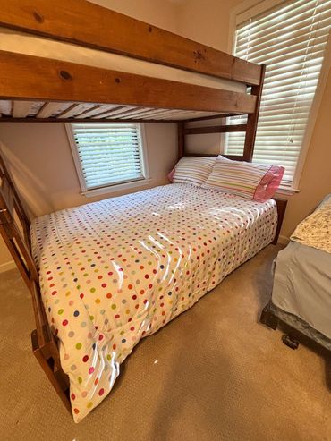 Cozy wooden bunk bed with colorful polka dot bedding in a sunlit room.
