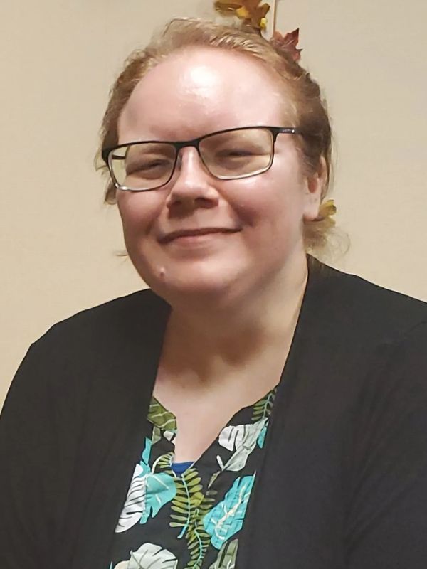 Smiling person with glasses wearing a black cardigan and floral shirt.