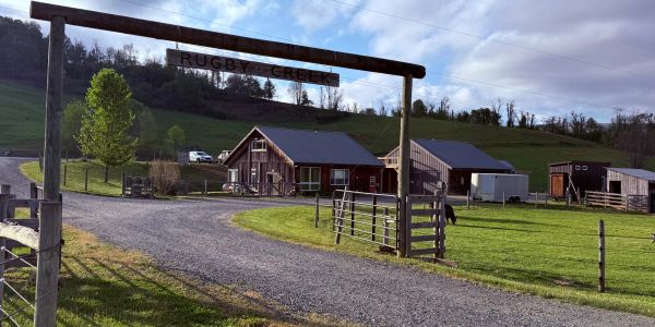Rustic farm entrance with wooden buildings and green fields.