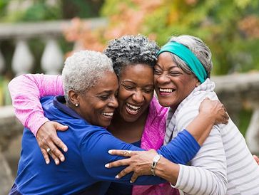 Three joyful older women sharing a warm group hug outdoors.