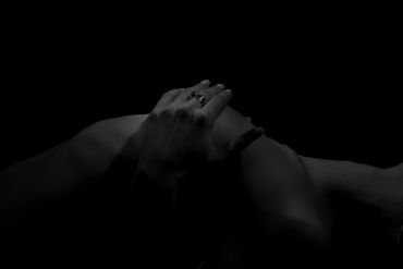 Black and white image of hands gently holding a knee in low light.
