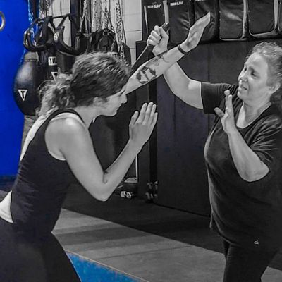 Two women practicing martial arts defense indoors.