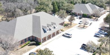 Aerial view of a suburban office complex with parked cars and surrounding trees.