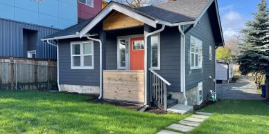 Small gray house with red door and green lawn.